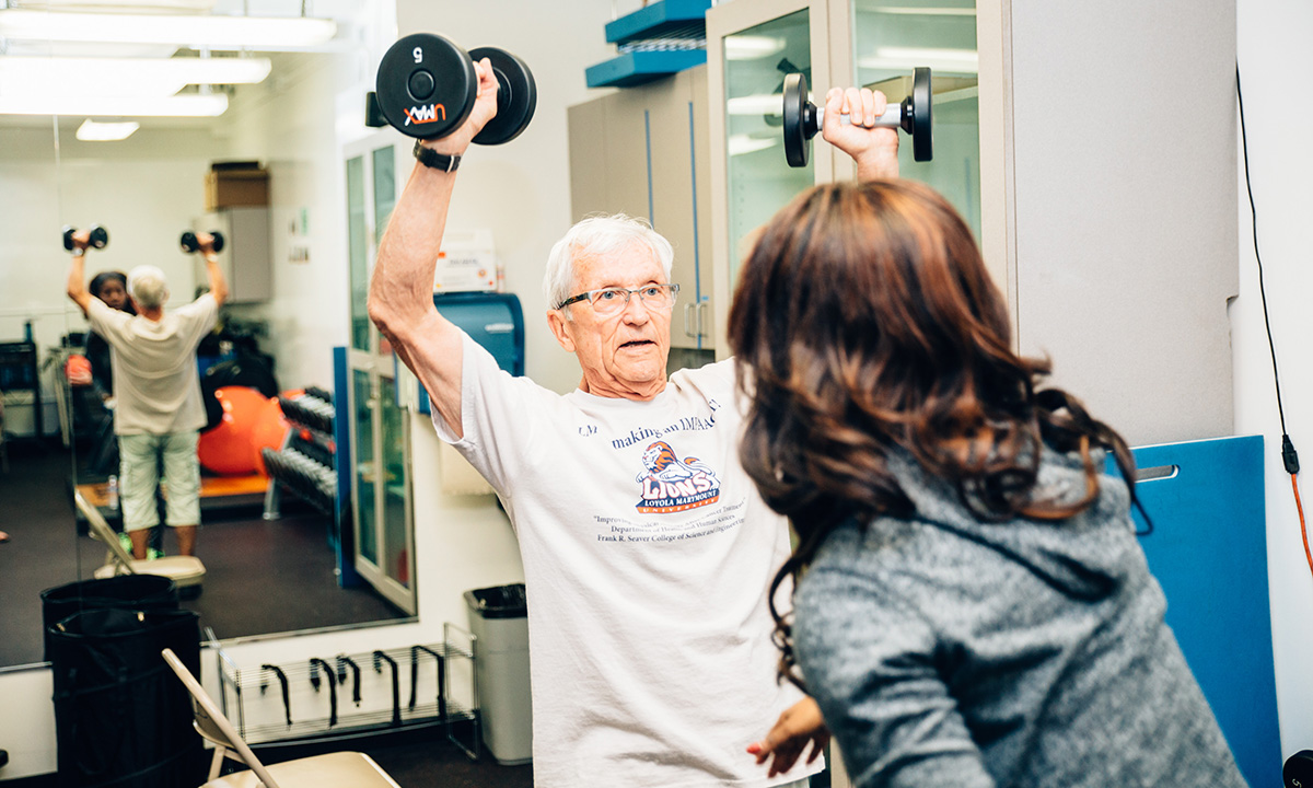 A personal trainer working with a senior staff member who is learning to properly lift weights