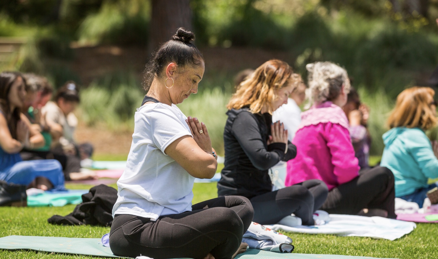A group of event attendees sitting outdoors in the grass while performing a meditation pose