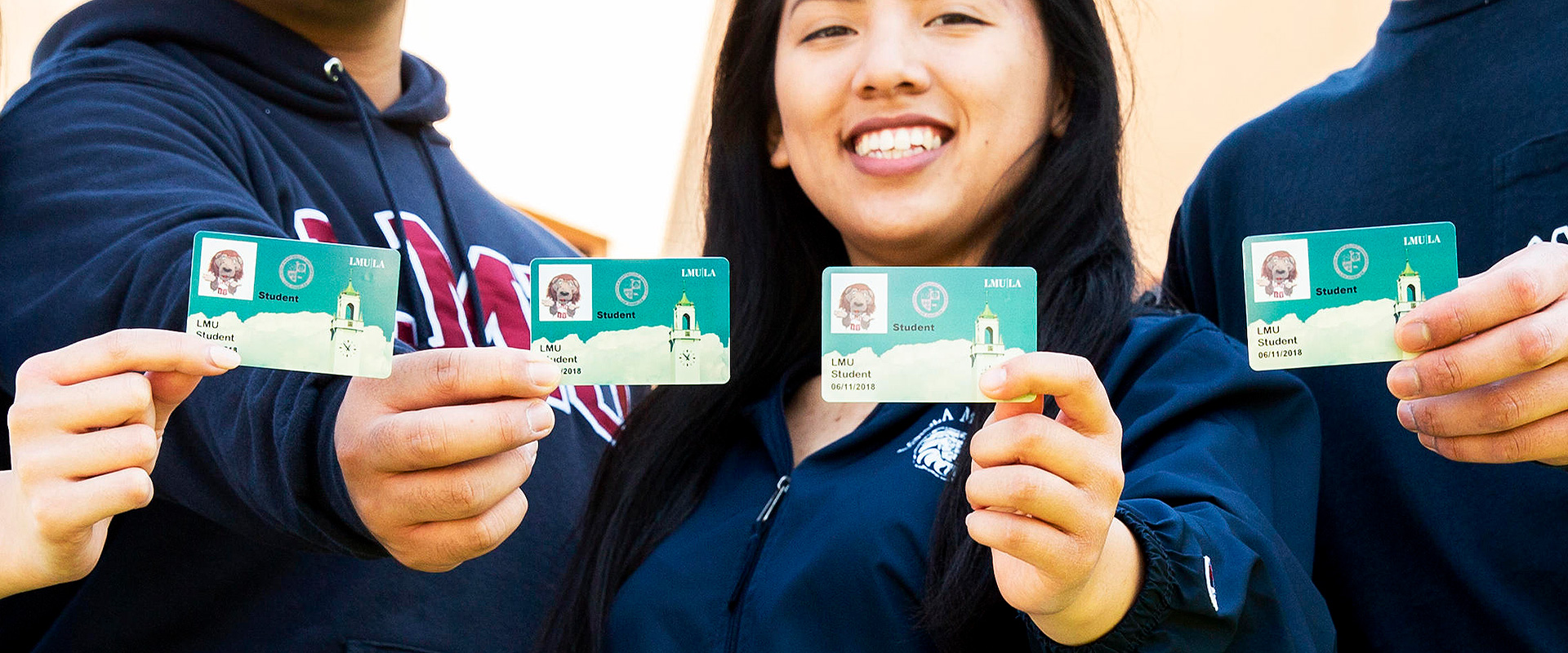 Four students holding up their OneCards to the camera