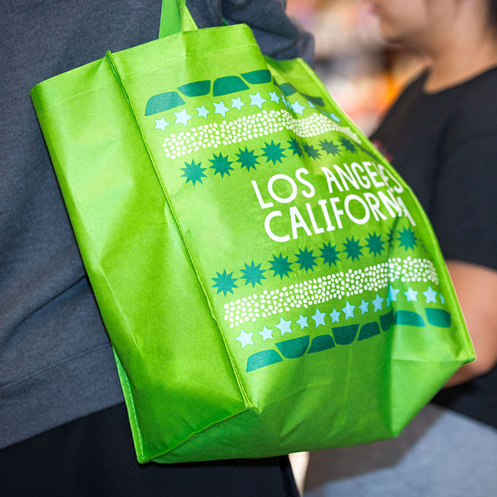 A student carrying a green reusable grocery bag with Los Angeles in white lettering.